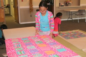 Brianna Jeffrie puts batting and backing on her quilt top during the quilting small group lead by Smallwood.